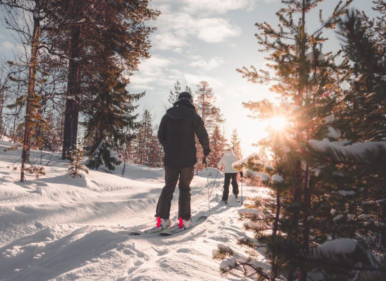 Two people cross country skiing on a snowy trail through the woods