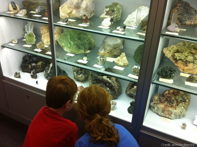 Two kids looking a gems and minerals on display behind a glass cabinet