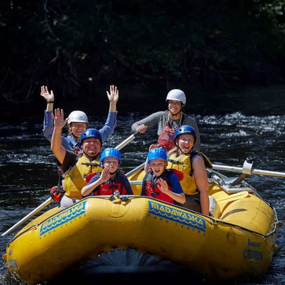 A group of people sitting in white water raft boat and smiling towards the camera