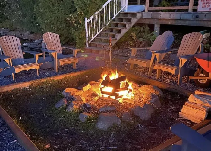A campfire surrounded by some nice Highlands chairs in front of stairs and a deck on a waterfront