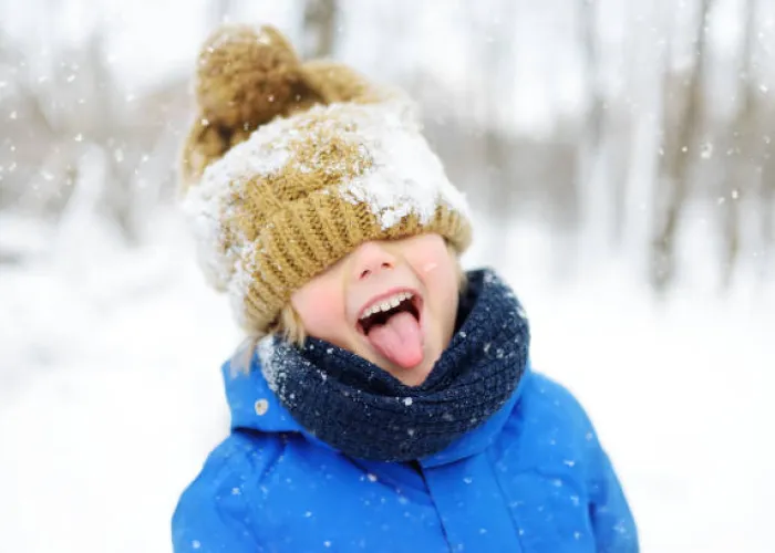 Young person catching snowflakes on their tongue, dressed in winter jacket and toque.