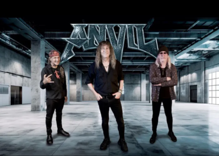 Anvil band picture - Three men standing in an empty warehouse with band name above them.