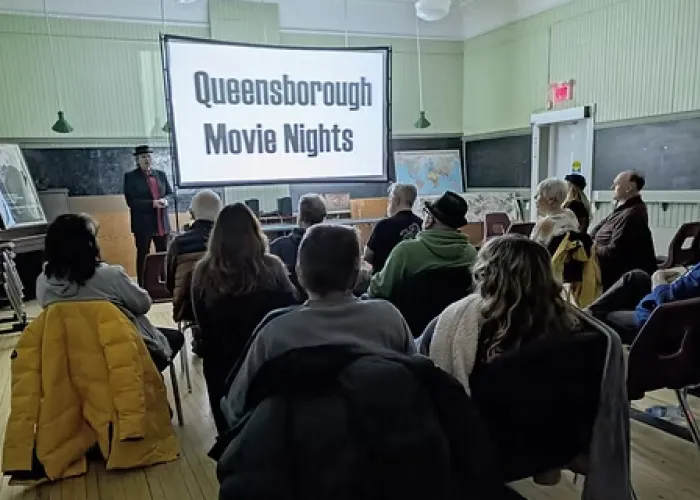 Group of people sitting in chairs in a room watching a screen with event title on it