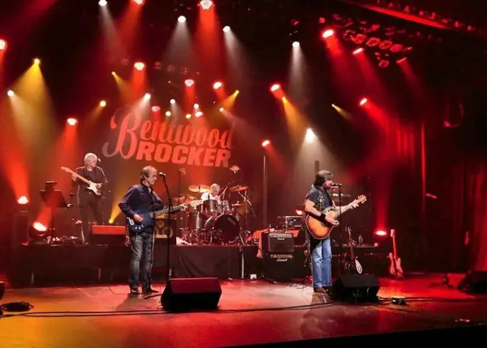 Photo of four members of band playing on stage bathed in red light, with Bentwood Rocker in white writing in background, three guitars and one drum set