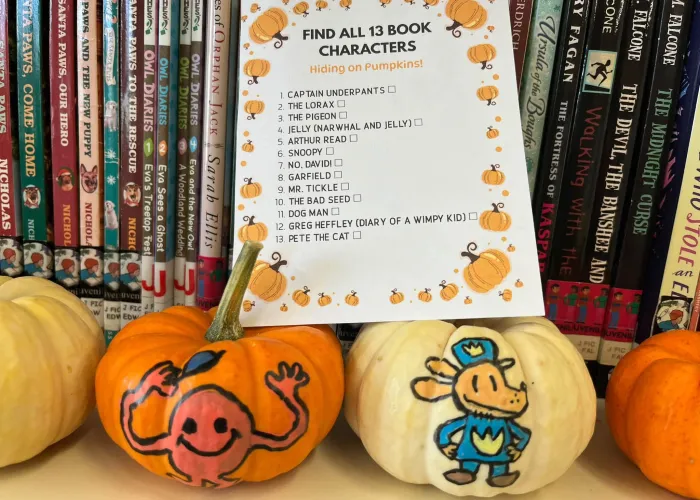 Photo of small pumpkins with characters drawn on them in front of a full book shelf, paper with a list of names and a pumpkin border on top of the pumpkins